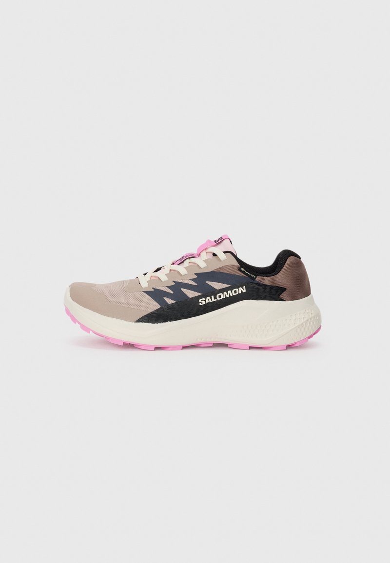 Chaussure de running Salomon beige et rose avec un motif en zigzag noir et une semelle blanche épaisse, vue de côté sur fond gris clair uni.