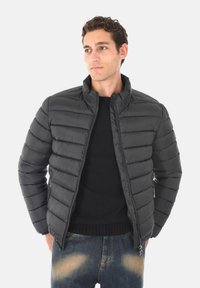 Giacca imbottita nera con design a cuciture verticali, colletto alto, zip frontale e polsini in maglia. Abbinata a jeans scuri con leggeri sbiadimenti.