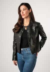 Zwarte leren jas met een kraag, drukknoopsluitingen en voorzakken. Gedragen over een zwart topje, gecombineerd met blauwe high-waisted jeans.