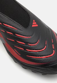 Juodas futbolo batelis su tekstūruota paviršiumi, raudonomis detalėmis ir guminėmis padais. Ypatybės - slip-on dizainas ir horizontalios juostelės šone.