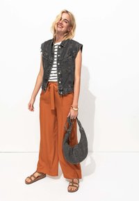 Gilet sans manches en denim noir, top à rayures, pantalon large orange avec ceinture, sac à main gris décontracté et sandales brunes à lanières.