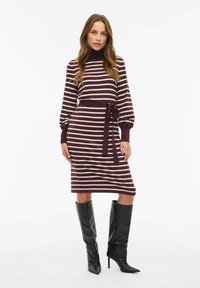 Kootud kleit bordo ja kreemjate triipudega. Kõrge mock kaelus, pikad varrukad, sidumisdetail vööl. Kombineeritud mustade, põlvikuni ulatuvate kontsadega saapatega.