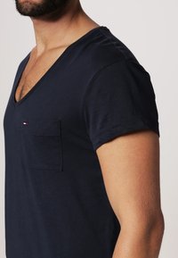 Granatowy bawełniany t-shirt z dekoltem w kształcie litery V, krótkimi rękawami i małą kieszonką na lewej piersi, ozdobiony szczegółem logo w trzech kolorach.