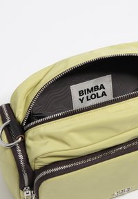 Yellow nylon bag with a zippered opening, featuring a brown zipper and silver hardware. Interior shows a label reading "BIMBA Y LOLA."