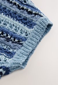 Gehäkelter, texturierter Stoff mit Blautönen in wechselndem Muster, mit einem gerippten Rand und einem offenen Gewebedesign.