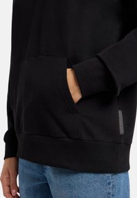 Schwarzer Hoodie mit einer Fronttasche, gerippten Bündchen und Saum sowie einem gewebten Etikett an der Seite. Hergestellt aus einem weichen, strapazierfähigen Stoff.