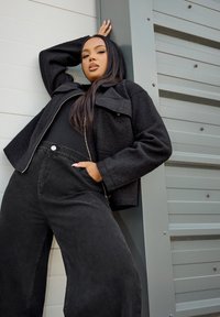 Svart fleecejacka med krage, dragkedjestängning och oversized passform, parat med hög midja på svarta vida byxor. Texturerade tyger synliga.