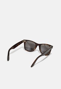 Lunettes de soleil écaille de tortue avec une monture carrée, verres foncés et accent doré sur les charnières. Texture lisse, branches courbées pour un bon ajustement.