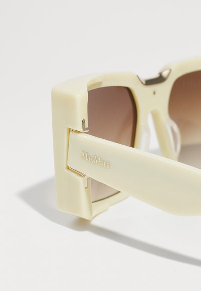 Beige ylisuuret aurinkolasit, joissa on tummanruskeat liukuvärilinsit. Paksut, kiiltävät varret, joissa on metallinen sarana ja "MaxMara"-logo painettuna.