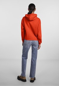 Röd huoodie, cropped design, mjuk textur. Bärs med ljusblå jeans, av avslappnad passform, synlig söm och fickor, samt bruna skor.