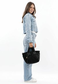 Borsa a tracolla nera trapuntata con doppi manici e una rifinitura in catena lucida; abbinata a una giacca di jeans cropped blu chiaro e jeans coordinati.