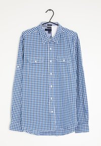 Camicia a maniche lunghe a quadri blu e bianchi con due tasche frontali e colletto classico, appesa a una gruccia nera. Materiale in cotone.
