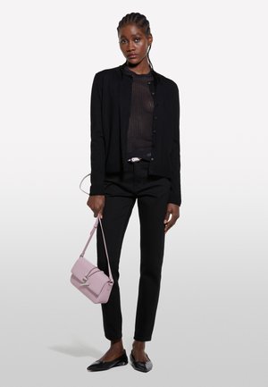 Black cardigan over a sheer black top, paired with black trousers and flat black shoes. A pale pink handbag with silver accents completes the look.