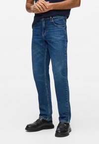 Pantalones vaqueros de denim azul con un diseño de pierna recta, que presentan un estilo clásico de cinco bolsillos y un ligero efecto de deslavado en la parte delantera.