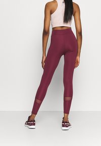 Leggings burdeos con cintura alta, con detalles de malla en la parte inferior de las piernas, fabricados con un material elástico para mayor flexibilidad.