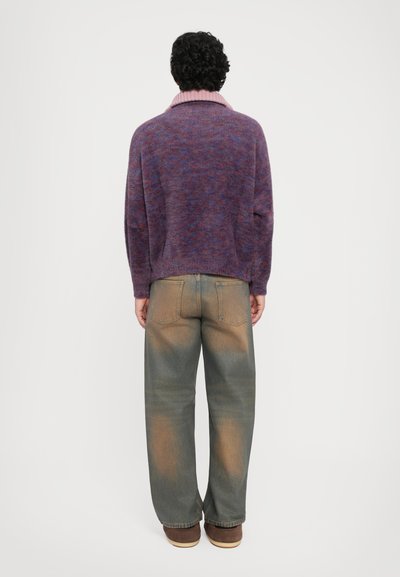 Knitted, purple sweater with high, pink collar; paired with wide, faded green jeans and brown shoes. View shows the back.