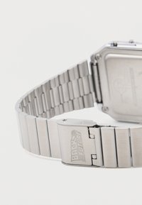 Ur i rustfrit stål med rektangulært urkasse, børstet finish og en rem med flade og ribbede led. Lås med indgraveringen "BACK TO THE FUTURE."