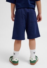 Mörkblå bomullsshorts med elastisk midja och en bakficka. Kombinerat med vita strumpor och gröna sneakers med vita detaljer.