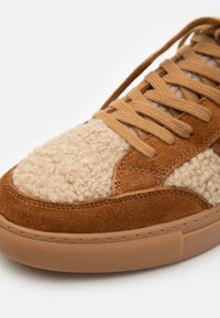 Baskets en daim marron avec une zone de bout en tricot texturé beige, lacets plats et semelle en caoutchouc à motif de losanges.