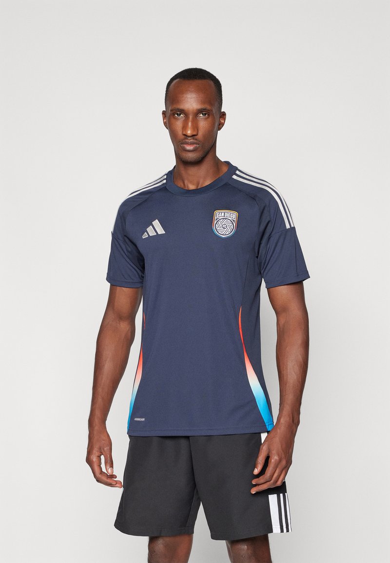 Jersey atlético de la Marina con mangas cortas, con acentos en degradado de rojo a azul, tres rayas blancas en los hombros y emblema de San Diego.