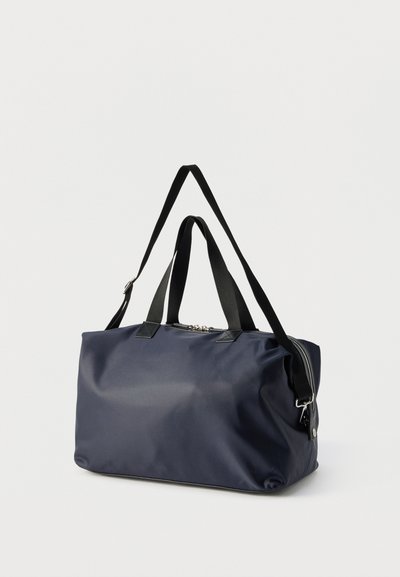 Ορθογώνια τσάντα duffel σε σκούρο μπλε χρώμα με μαύρες λαβές και ρυθμιζόμενο ιμάντα ώμου, ασημένιο φερμουάρ, σε απλό ανοιχτό φόντο.