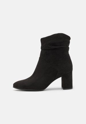 Fekete velúr boka csizma, laza felső résszel, hegyes orral és vastag blokk sarkával. Simább textúrájú, további minták vagy kiegészítők nélkül.