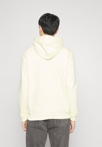 Lichtgele hoodie met een touwhals, geribbelde manchetten en een geribbelde zoom. Gemaakt van zachte stof met een gladde textuur. Gezien van achteren.