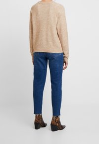 Pullover beige a maglia con orlo a coste, abbinato a jeans in denim blu con gamba dritta e stivaletti alla caviglia in pelle con motivo a serpente in nero e marrone.