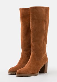 Botas altas de ante marrón con puntera redondeada, tacón cuadrado y superficie texturizada; presenta costuras verticales a lo largo de los lados.