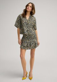 Twee-delig leopardprint outfit met een kortmouwtop en een gelaagde rok, gemaakt van lichte stof. Gele hoge hakken inbegrepen.