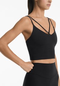 Black cropped tank top with thin, crisscross straps, a v-neck design, and smooth texture. Paired with high-waisted, black leggings.