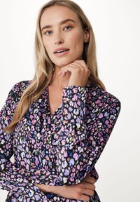 Blouse noire à motif floral présentant des nuances de rose, de violet et de bleu, avec des manches longues et un décolleté en V.