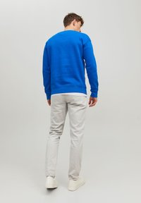 Sweatshirt bleu avec des poignets et un ourlet côtelés, associé à un pantalon tapered gris clair et des baskets blanches, vu de dos.