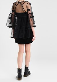 Czarny przezroczysty top z rozszerzanymi rękawami, kwiatowym haftem, warstwowym wzorem na dopasowanej czarnej sukience, zestawiony z czarnymi botkami sięgającymi kostek.