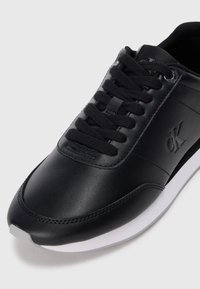 Sneaker in pelle nera con lacci neri e suola bianca, caratterizzata dal logo "CK" in rilievo sul lato.