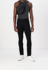 Black denim jeans with slim fit, paired with a gray sleeveless shirt and a black crossbody bag. White sneakers complete the look.