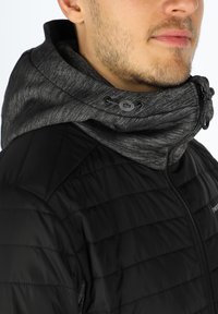 Giubbotto imbottito nero con colletto alto, dotato di cappuccio grigio texture, cordino di regolazione e dettaglio con zip.