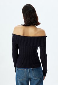 Rippstrick-Off-Shoulder-Pullover in Dunkelblau, mit enger Passform und langen Ärmeln. Kombiniert mit hochgeschnittenen Jeans, die einen lässigen Stil zeigen.