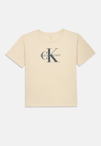 Krátký rukáv, krémové bavlněné tričko se velkým šedým logem "CK" a textem "Calvin Klein" níže. Klasický design s kulatým výstřihem.