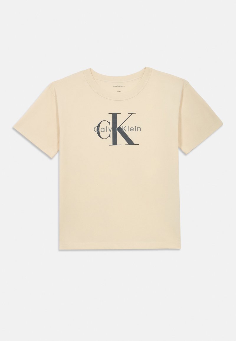 Krátký rukáv, krémové bavlněné tričko se velkým šedým logem "CK" a textem "Calvin Klein" níže. Klasický design s kulatým výstřihem.
