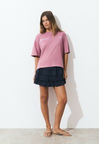 Pink cotton oversized t-shirt with "GALAXY CODE" text, paired with a navy ruffled mini skirt and beige flip-flops. Smooth textures visible.