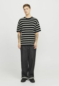 Sort-hvid stribet kortærmet t-shirt, løst fit, kombineret med mørke bredbenede jeans og sorte sko. Ensfarvet hvid baggrund.