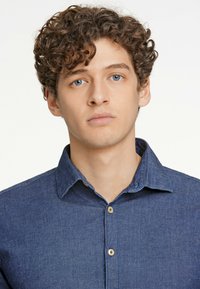 Camicia in denim blu scuro con colletto a punta e un tessuto testurizzato. Due bottoni visibili sulla parte anteriore.