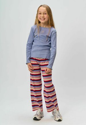 Tricou cu mânecă lungă, cu dungi, de culoare albastru deschis, având o margine volanată, asortat cu pantaloni largi cu dungi în diverse culori. Adidașii finalizează ținuta.