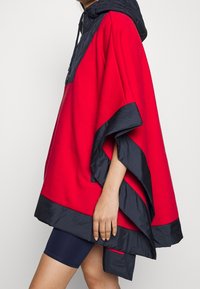 Röd och marinblå poncho med huva, med en texturerad överdel och slät nedre kant, lös passform med sidöppningar.