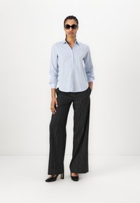 Camicia a righe blu chiaro con bottoni, pantaloni larghi a righe verticali neri, tacchi neri e occhiali da sole scuri. Panno morbido, vestibilità su misura.