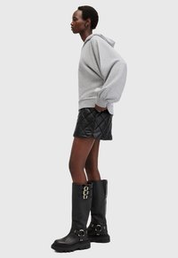 Felpa grigia oversize con polsini elasticizzati, abbinata a una mini gonna nera trapuntata e stivali neri alti con dettagli in oro.