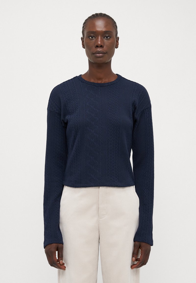 Pull en maille bleu marine avec un motif texturé, col rond et manches longues. La coupe est légèrement cropped à la taille.