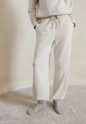 Light beige sweatpants made of soft fabric with an elastic waistband and drawstring. Features side pockets and a tapered leg design.