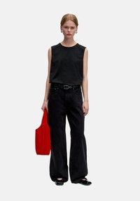 Zwarte mouwloze top, hoogprojecterende zwarte denim wijde jeans, zwarte schoenen en een rode tote bag met een afgeronde bovenrand. Casual outfit.